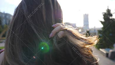 Unrecognizable dark haired woman standing at urban street and straightening hair. Girl standing at city environment with
