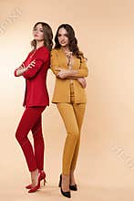 Two gorgeous models in colored suits and high heels over flat background.