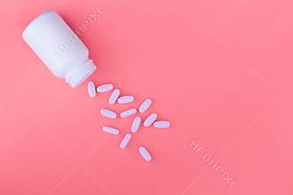 Bottle of medicines and scattered pills on a pastel pink background. Ripped vitamins on a bright background