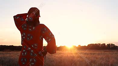 Rear View of African woman in traditional clothes standing in a field of crops at sunset or sunrise
