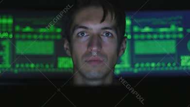 Man hacker programmer working at computer while green code characters reflect on his face in cyber security center