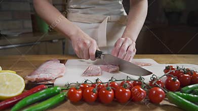 The cook slices raw fish before cooking seafood meal, tomatoes with pepper and raw fish, cooking fish, asian cuisine