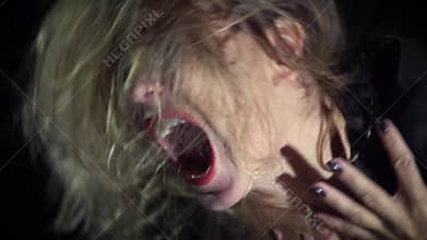 Witch with disheveled hair and black nails screaming in the dark, slow motion shooting