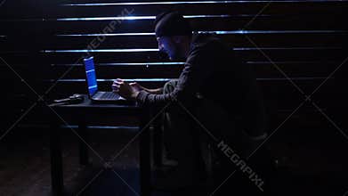 Comic funny hacker commits a cyber attack with a laptop and a gun in his hands