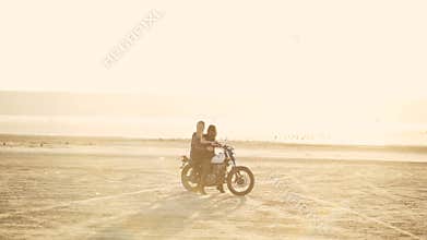 Attractive young woman motorcyclist with his girlfriend riding a motorcycle in a desert on sunset or sunrise. Girlfriends on a bik