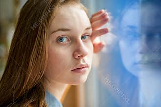 Young depressed lonely female college student standing by a window at her school, looking at the camera. Bullying concept.