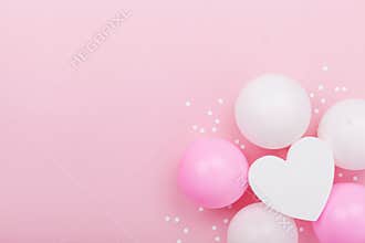 Birthday or wedding mockup with white heart shape, confetti and pastel balloons on pink table from above. Flat lay composition.