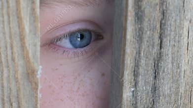 Boy teenager peeking into the crack in fence or doorway close up view