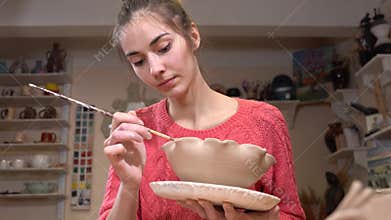 General view of a female ceramist smoothing the clay pot edges using the tassel in the pottery workshop.