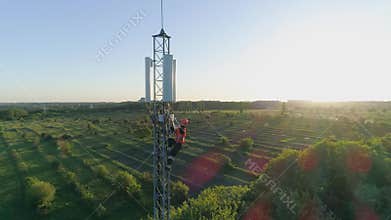 Maintenance worker carry out repairs high up on communications tower using safety equipment on background of sunset