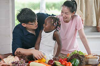Asian couple cooking and tasting food with african american girl together in kitchen at home