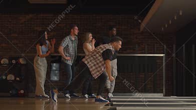A young Caucasian man makes the final throw with a bowling ball and wins the game with the support and joy of his