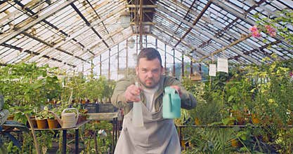 Funny young man in a greenhouse shoots water at the camera like a cowboy in the wild west.