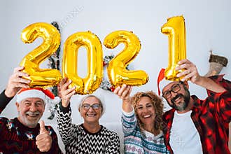 Four people having fun and smiling together at home holding up the four balloons numbers of the 2021 - family laughing and