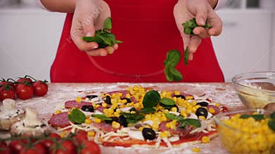 Hands scatter basil leaves on pizza - slow motion