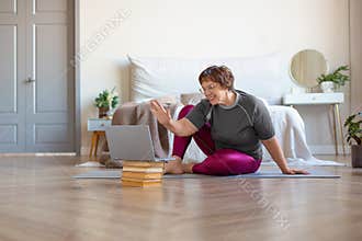 An older woman communicates with a trainer online before a Pilates workout.