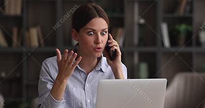 Unhappy young woman holding unpleasant telephone conversation, working on computer.