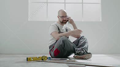 Builder with glasses calls on mobile phone sitting on floor