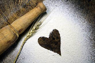 Fresh harvested wheat grain on wheat flour background. Baking concept on wood background, sprinkled flour with heart.