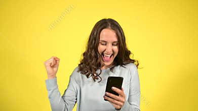 Attractive curly young woman using smartphone isolated on yellow