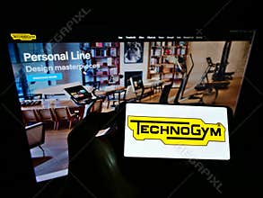 Person holding cellphone with logo of Italian fitness equipment company Technogym SpA on screen in front of business website.