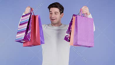 Handsome man holds shopping paper bags on violet studio background. Guy bought presents on sales with discounts.