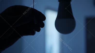 A Person Pulls the Switch Cord with His Hand and Turns Off the Light Bulb. Turning Off the Led Light in the Office Room.