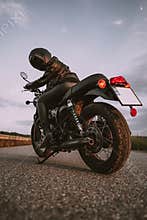 Stylish motorcyclist woman in helmet and leather jacket sitting on vintage motorcycle. Female driver outdoors on nature