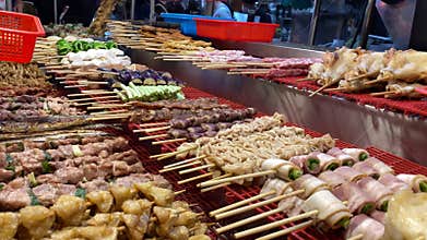 Vendor selling Taiwanese chicken on skewers, steel grill night market street