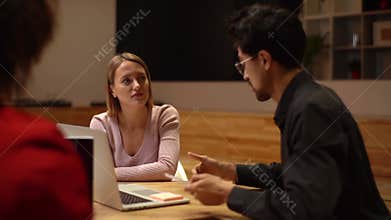 Young team leader sitting at table with multiethnic colleagues, discussing working issues at negotiations meeting.