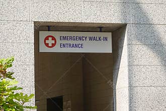 Sign over a doorway to an emergency room that says emergency wail in entrance with a white and red cross logo
