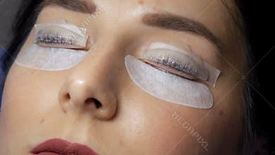 Face of a young girl in a modern eyelash lamination procedure in a professional beauty salon. The master applies a