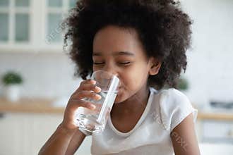 Pretty little African American girl drinking fresh water in kitchen