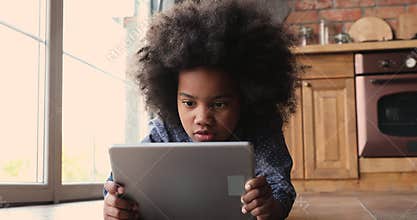 Little african girl lying on warm kitchen floor with tablet