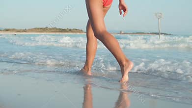 Unknown girl enjoying summer at beach. Slim woman legs walking at coastline.