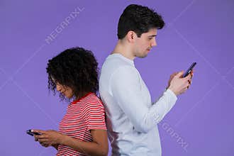 Interracial couple stand with their backs to each other and print messages or surf Internet from mobile phones