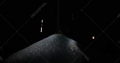 Small granules of sugar fall into glass container at darkness