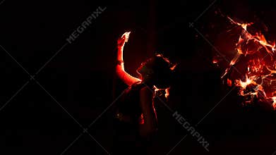 the silhouette of a woman looking at her jewelry with a face full of sadness and the fire burning around her