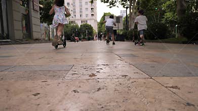 Children riding scooters along a vibrant city pathway in the afternoon.