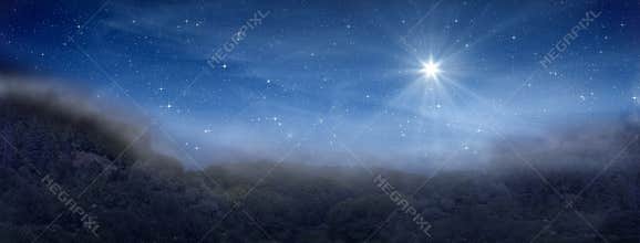 Bright star indicates the Nativity of Jesus Christ in the starry sky and fog rises in the mountains above the night forest