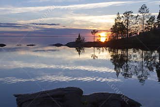 Silhouettes of rocky shoreline and trees against the backdrop of sunset over the lake