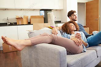 Couple Relaxing On Sofa With Hot Drink In New Home