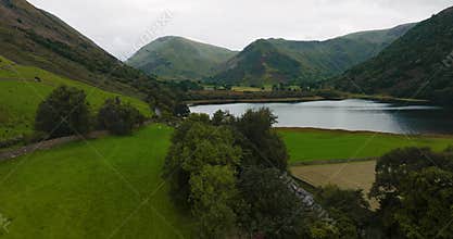 Bird-eye's view of white electric car driving the road in beautiful lakeside countryside in England.
