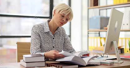 Thoughtful woman turns pages of planner at computer