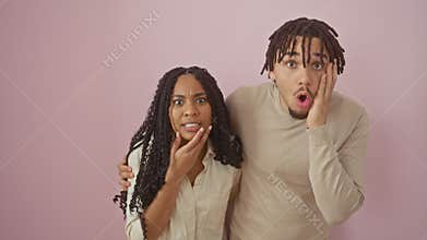 Stunning couple, mouth wide open in disbelief, standing amazed over an isolated pink backdrop, their faces a mix of shock and