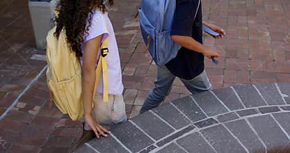 Teen students walking across brick plaza wearing backpacks with sunlight drawing them to bench