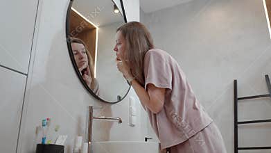 Woman looks at reflection while checking face skin near bathroom sink