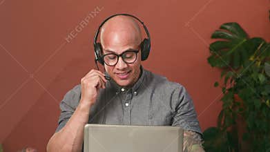 Smiling Bald Man Engaged in an Online Call While Working Remotely From Home with a Headset