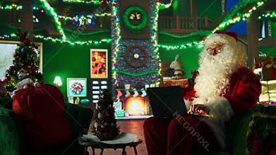 Man portraying Christmas character amused by children wish lists on laptop