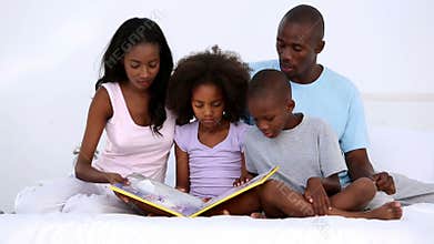 Family reading book on bed